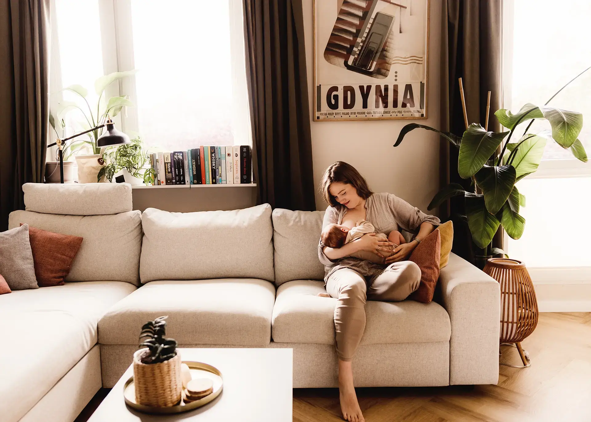 Mama Agnieszka karmiąca piersią noworodka Jerzyka w przytulnym salonie, sesja noworodkowa lifestyle w Gdyni, naturalne światło i nowoczesne wnętrze
