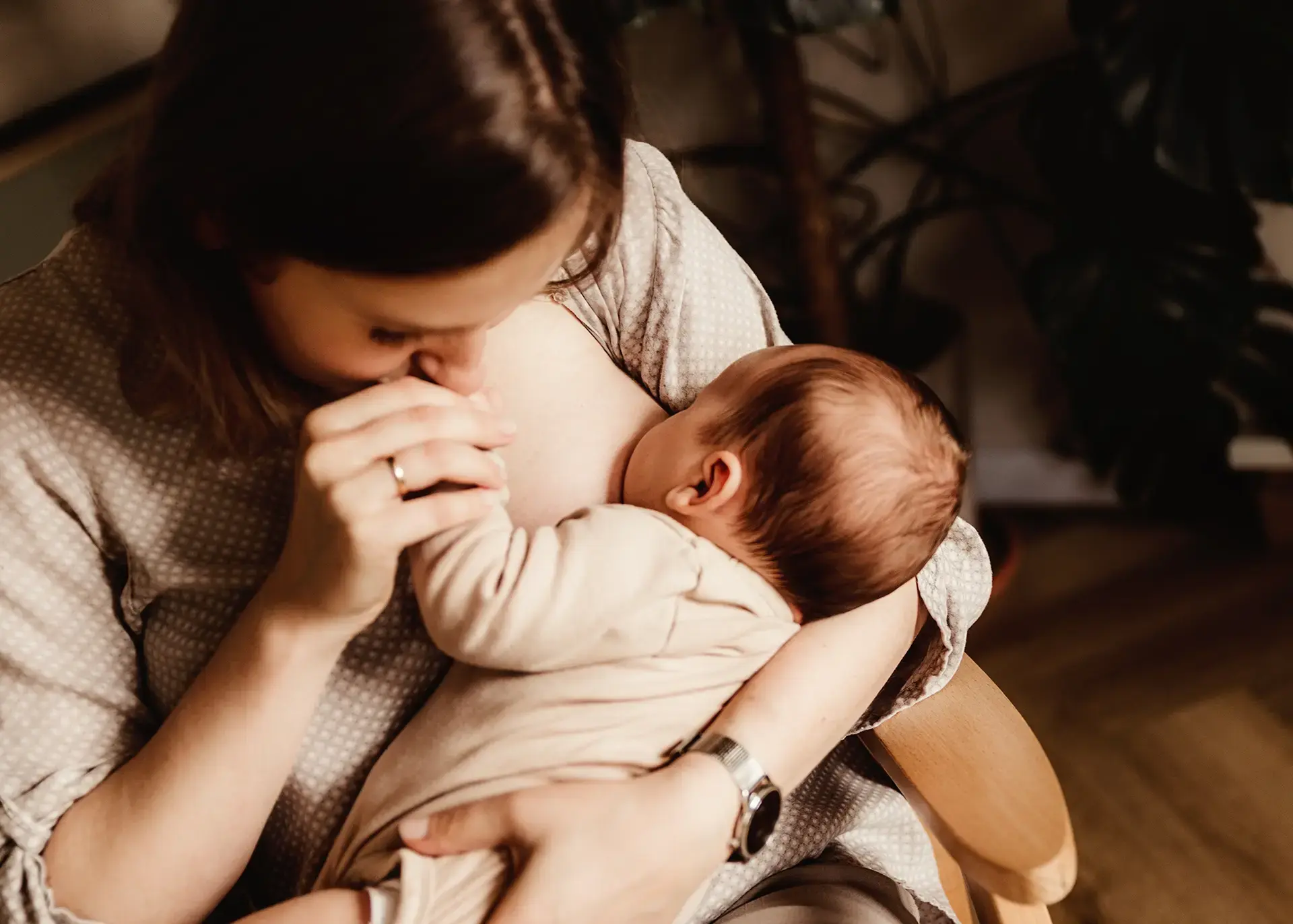 Zbliżenie na mamę Agnieszkę karmiącą noworodka i całującą go w rączkę, intymna sesja noworodkowa w domu, Jerzy i Agnieszka, naturalna fotografia lifestyle Gdynia