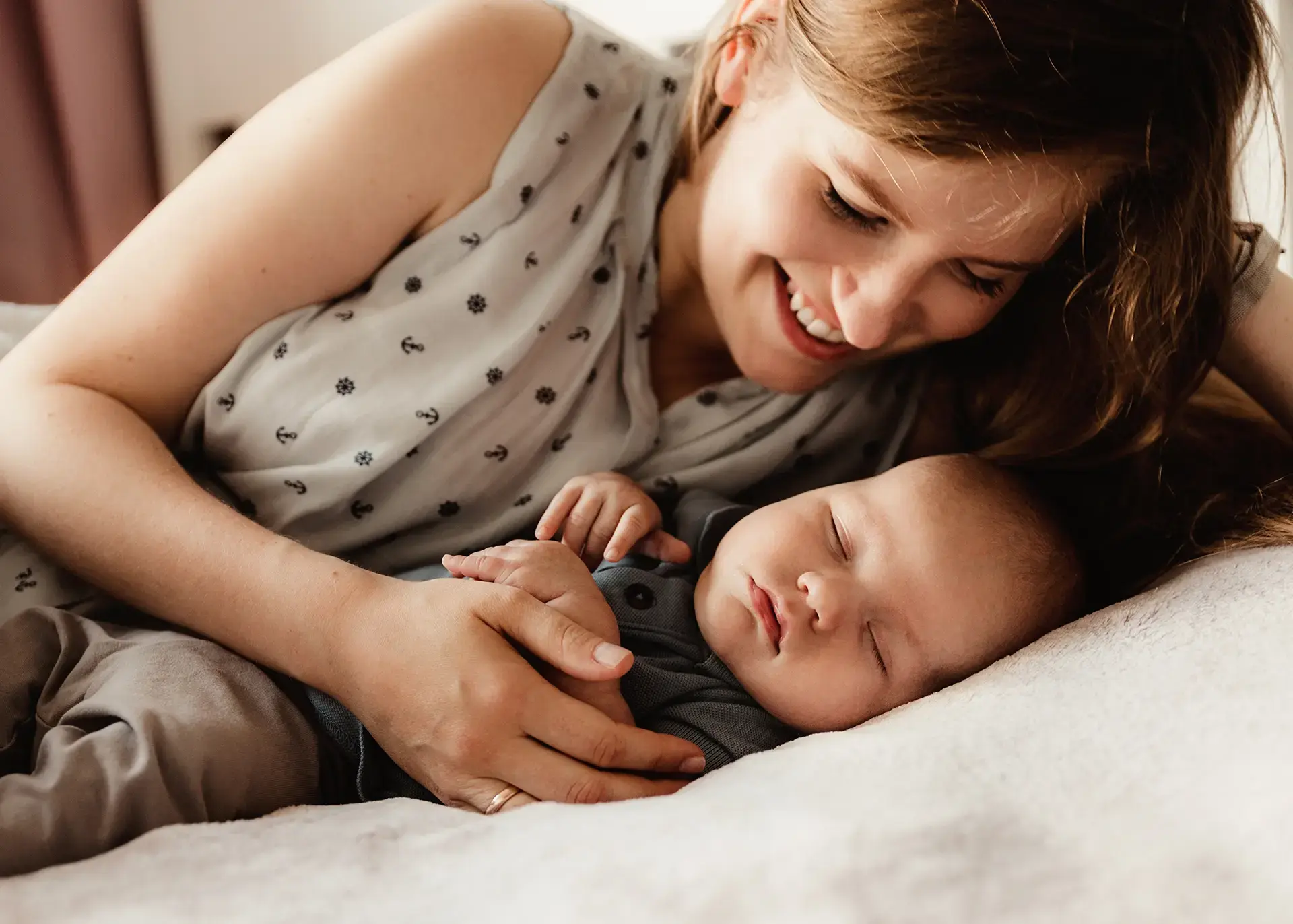 Czuła domowa sesja noworodkowa, mama Agnieszka uśmiecha się do śpiącego synka Jerzyka, naturalny portret mamy i dziecka na łóżku, fotografia rodzinna Rumia