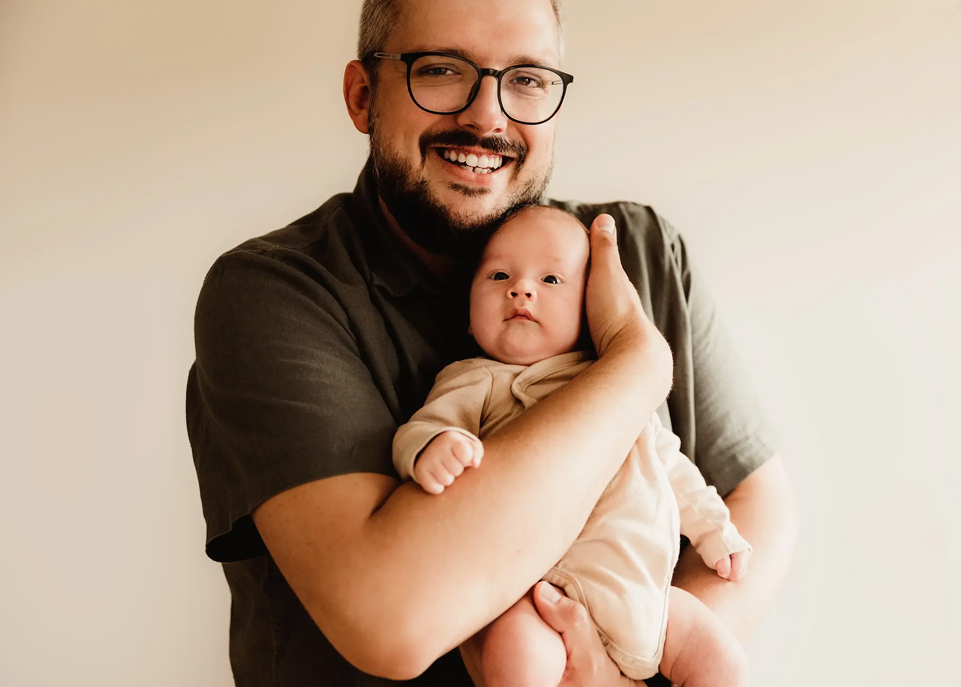 Dumna mina taty Krzyśka trzymającego w ramionach małego Jerzyka, uśmiechnięty ojciec z noworodkiem, domowa sesja lifestyle w Gdyni, naturalna fotografia rodzinna