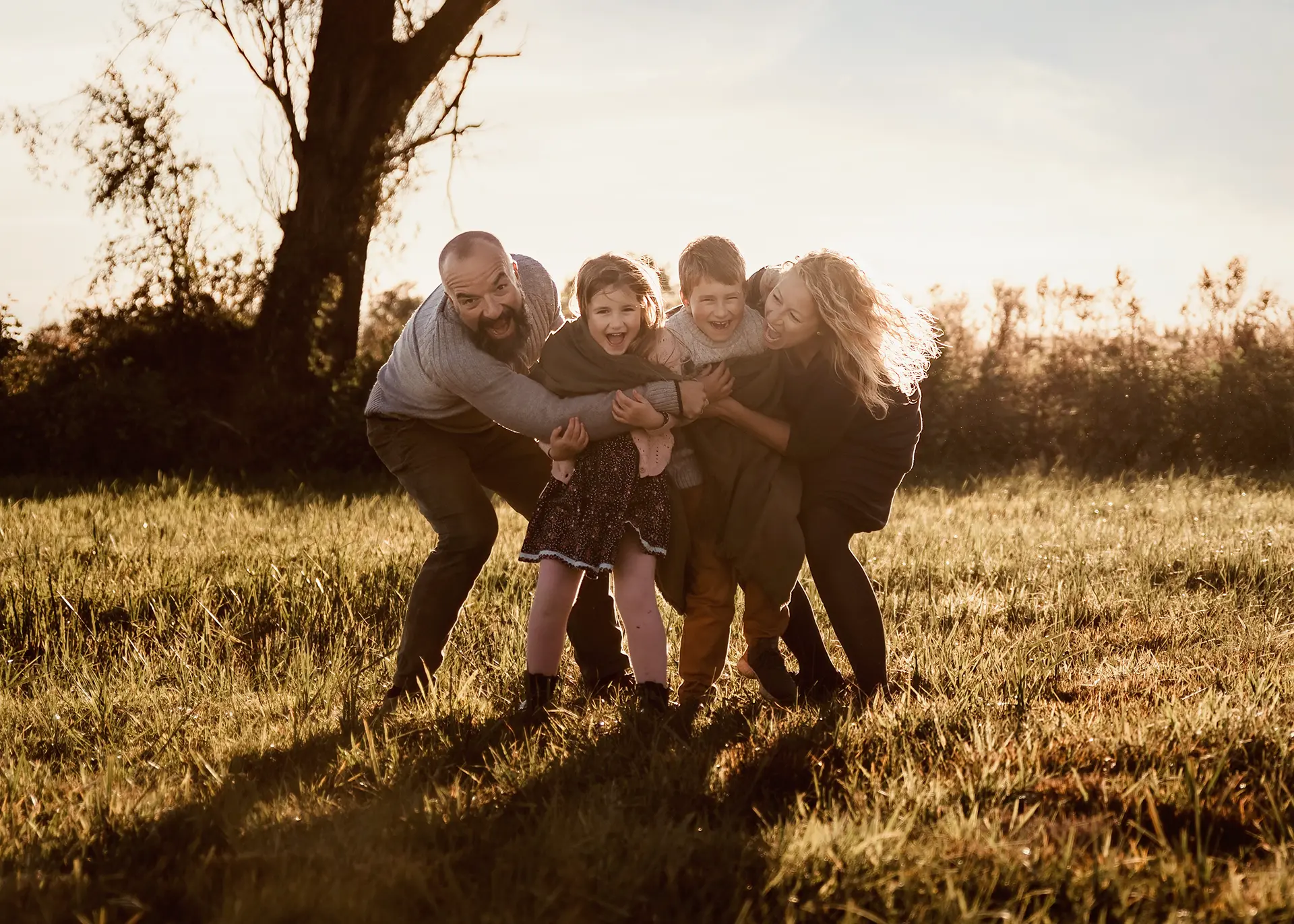 Radosna rodzina z dwójką dzieci biegnąca po łące w stronę obiektywu, złota godzina, naturalna sesja rodzinna w Gdańsku, fotografia lifestyle