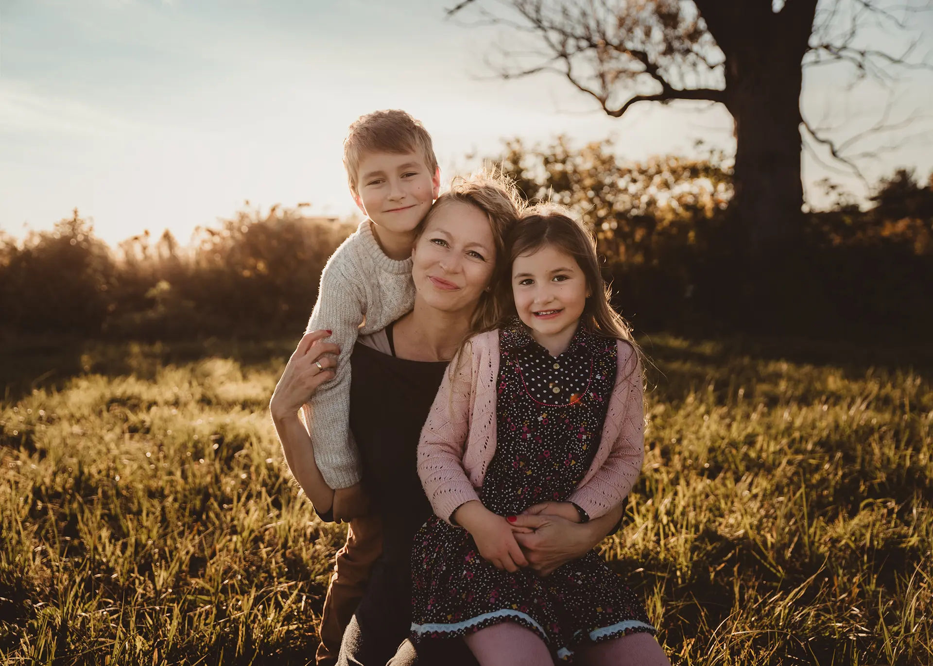 Ciepły portret mamy z synem i córką podczas sesji rodzinnej w plenerze, złota godzina, naturalne uśmiechy i bliskość, fotograf rodzinny Reda