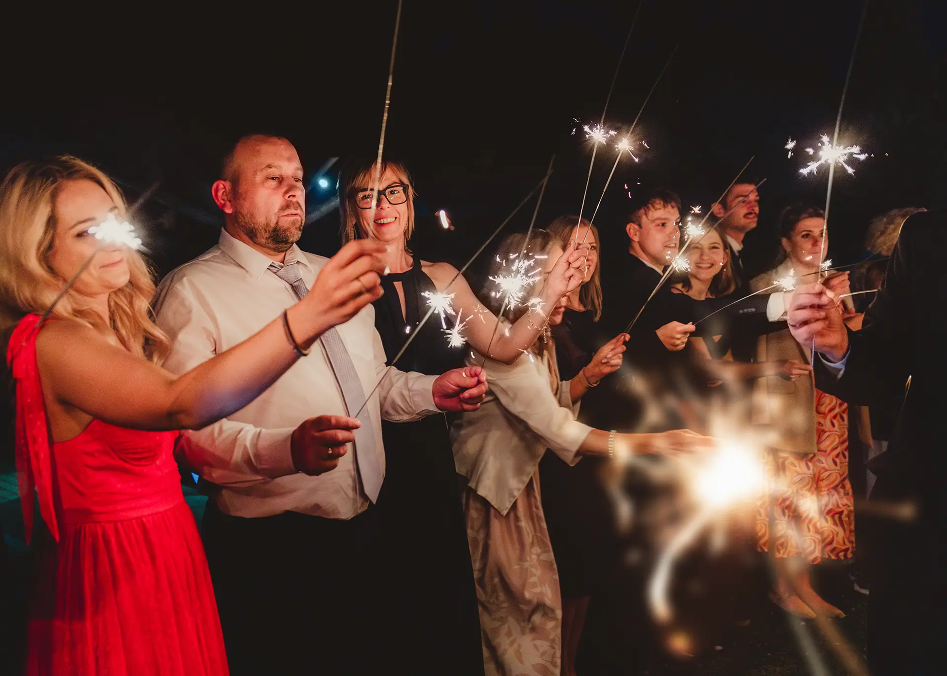 Kolorowa fotografia ślubna nocą, roześmiani goście weselni trzymający zapalone zimne ognie, atrakcje dla gości na weselu, fotograf Gdynia