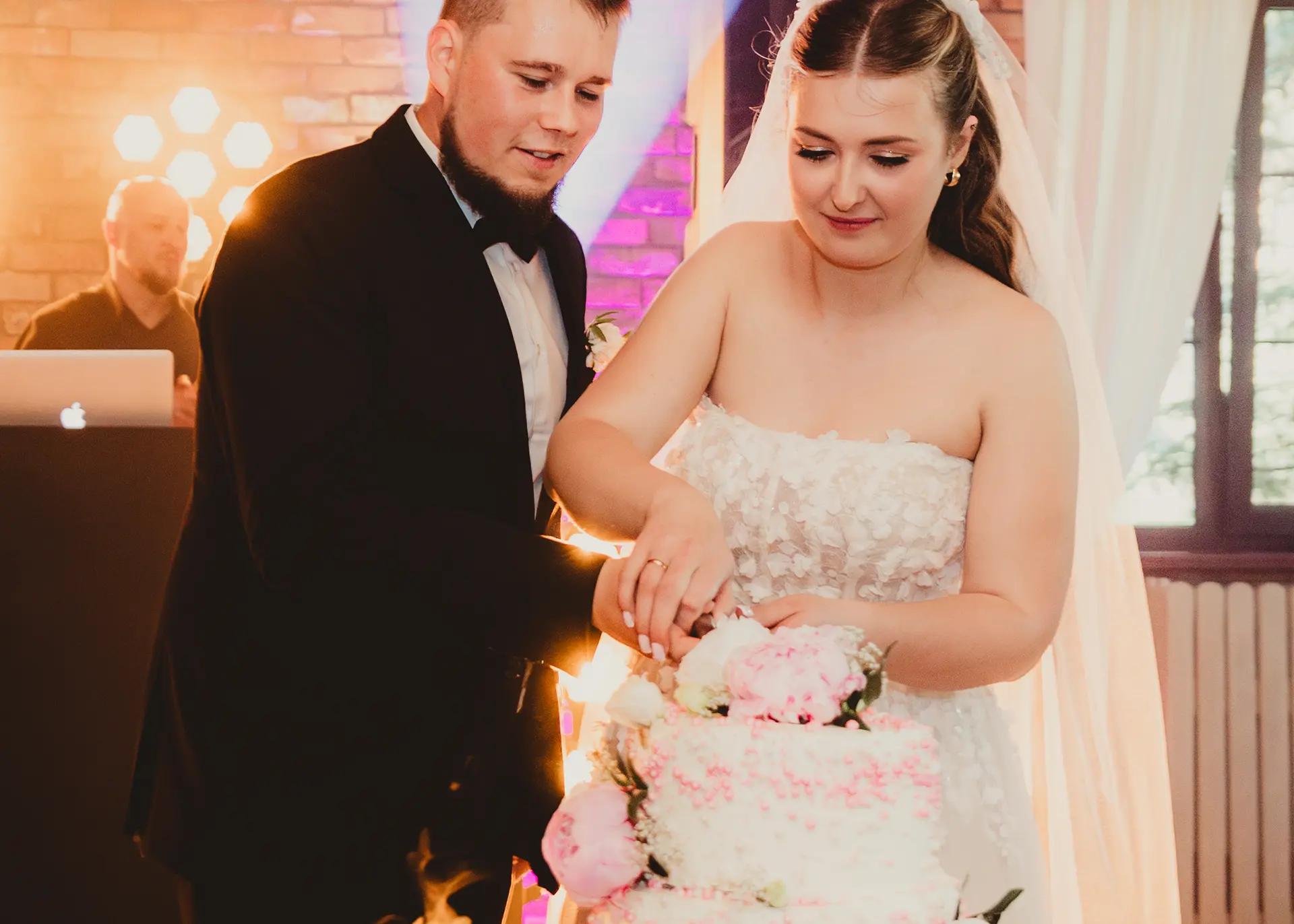 Kolorowa fotografia ślubna, panna młoda i pan młody wspólnie krojący trzypiętrowy biało-różowy tort weselny, radosny moment na sali weselnej, fotograf Rumia