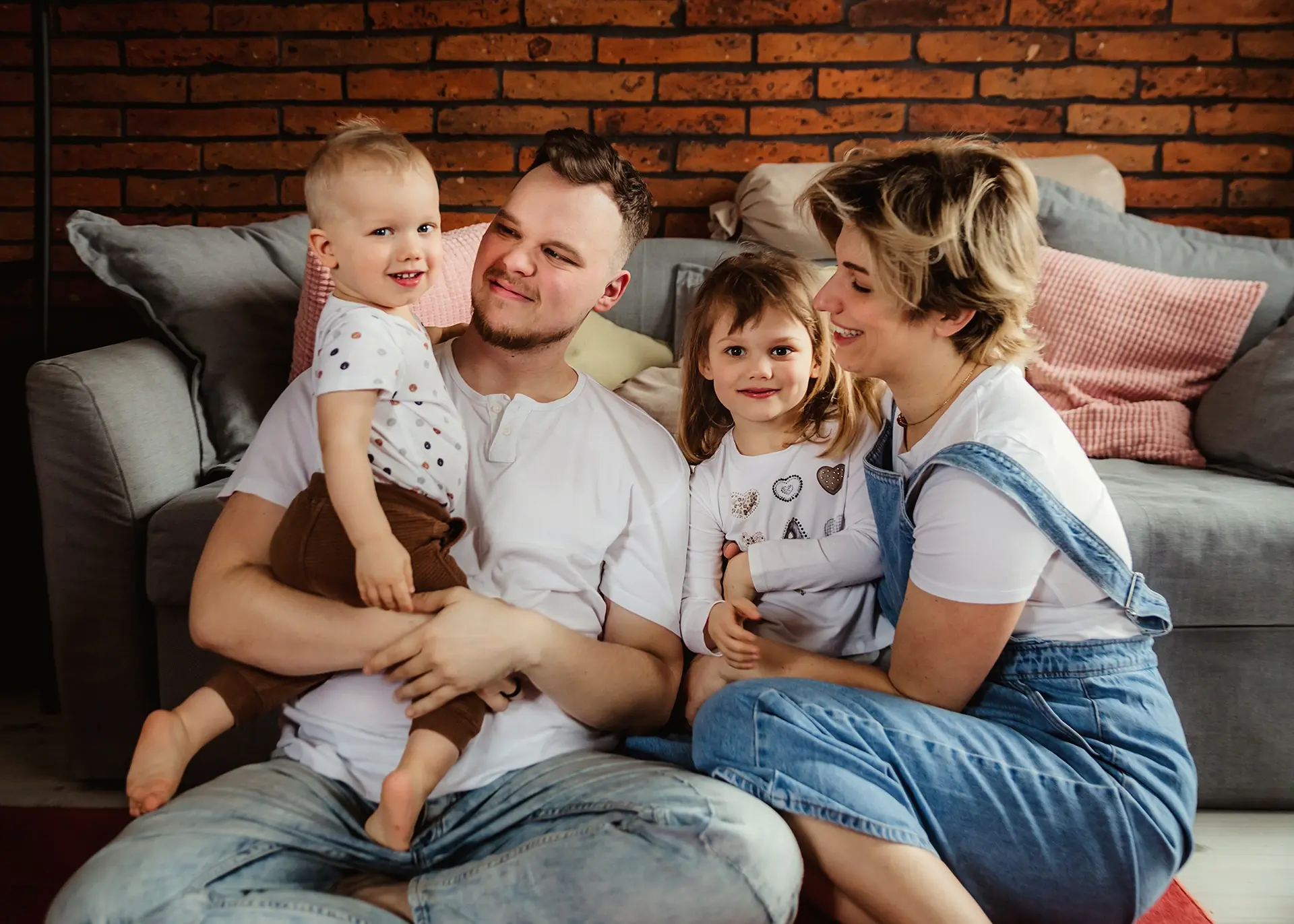 Rodzina z dwójką dzieci podczas sesji domowej na tle ceglanej ściany, radosna opinia o fotografie