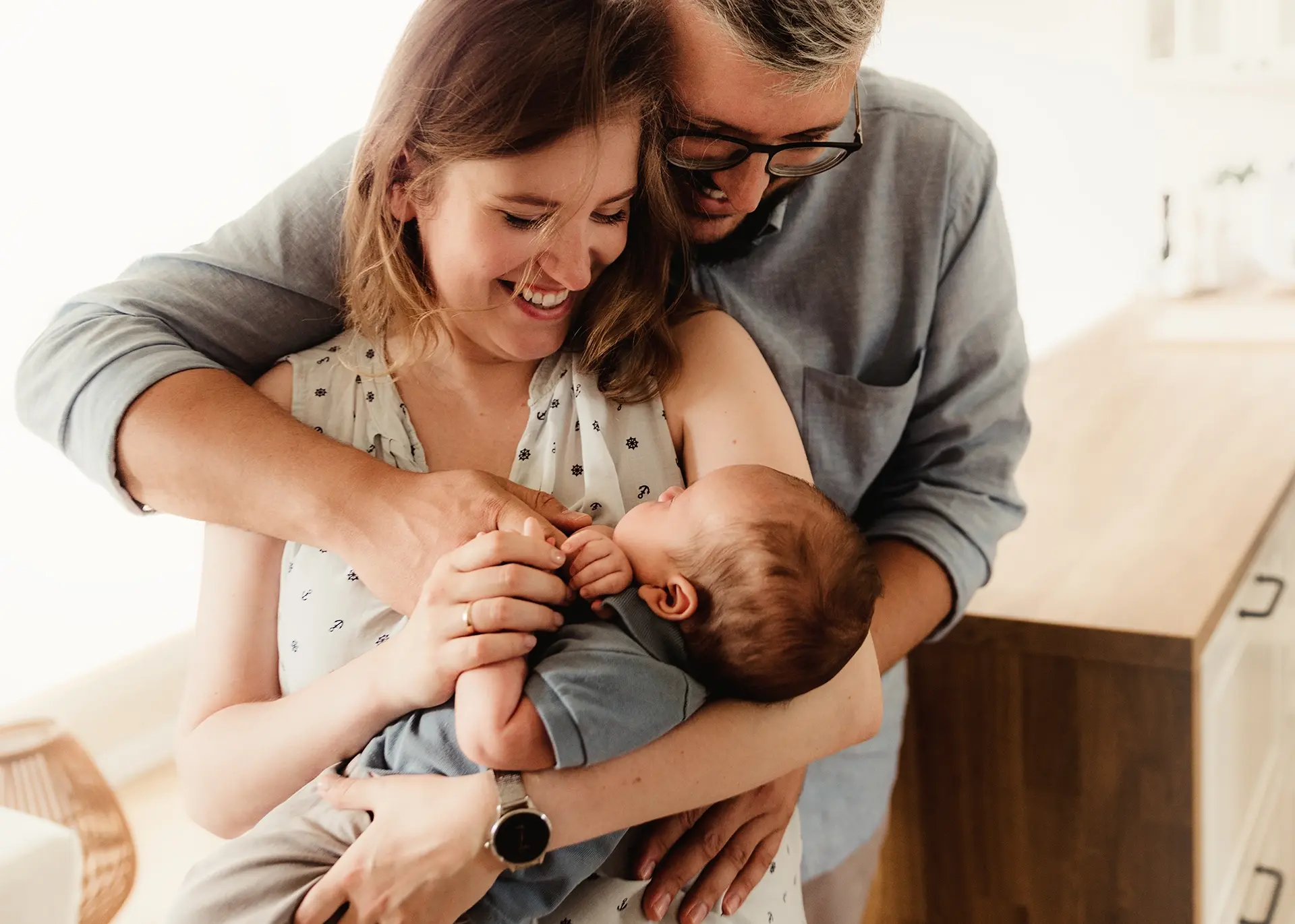 Uśmiechnięci rodzice trzymający noworodka podczas domowej sesji zdjęciowej typu lifestyle